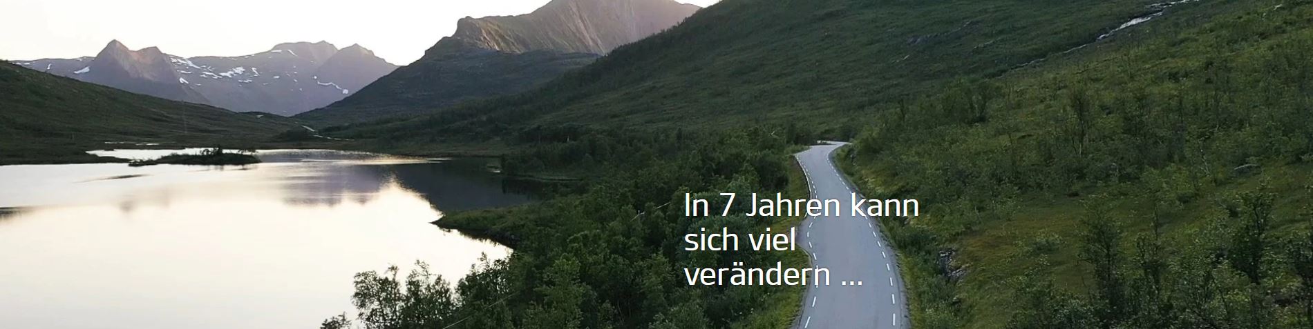 Grüne Landschaft mit einem See und in der Mitte verläuft eine Straße